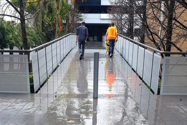 workmen pushing wheelbarrow down a pedestrian bridge